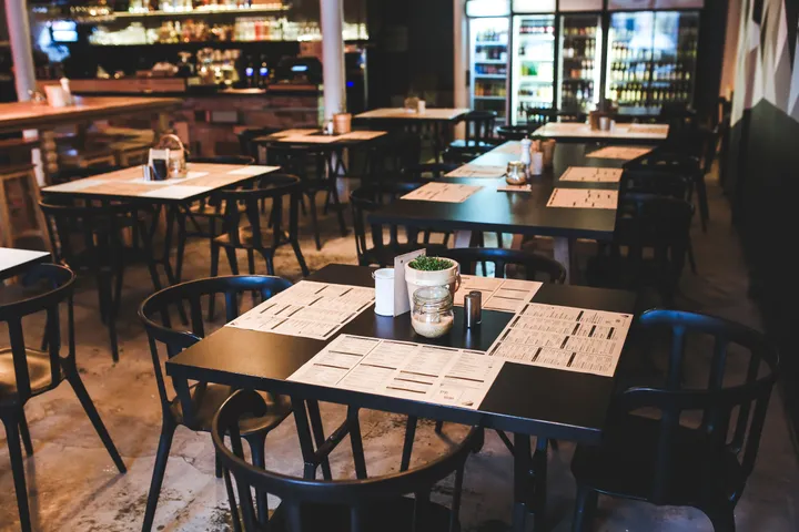 Salle de restaurant avec tables dressées de menus et bar en arrière-plan, avant le service.