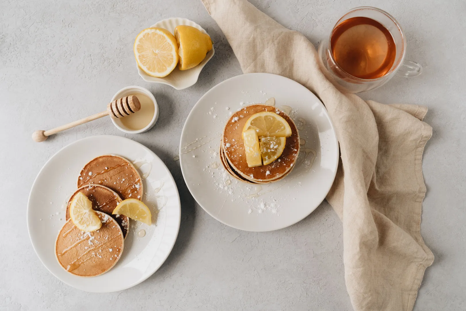 Assiettes de pancakes au miel et au citron accompagnées d'un thé, dressées pour un service petit-déjeuner ou brunch.