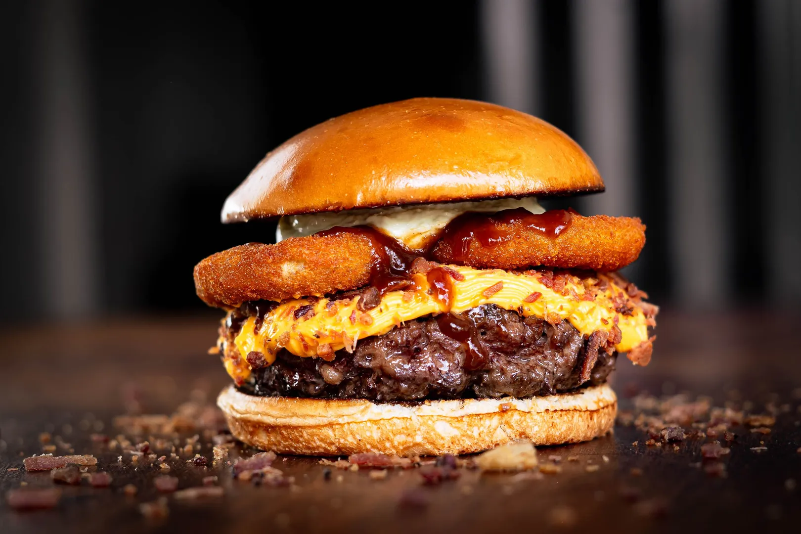Gros plan sur un burger gourmet avec cheddar fondu, onion rings et sauce barbecue.