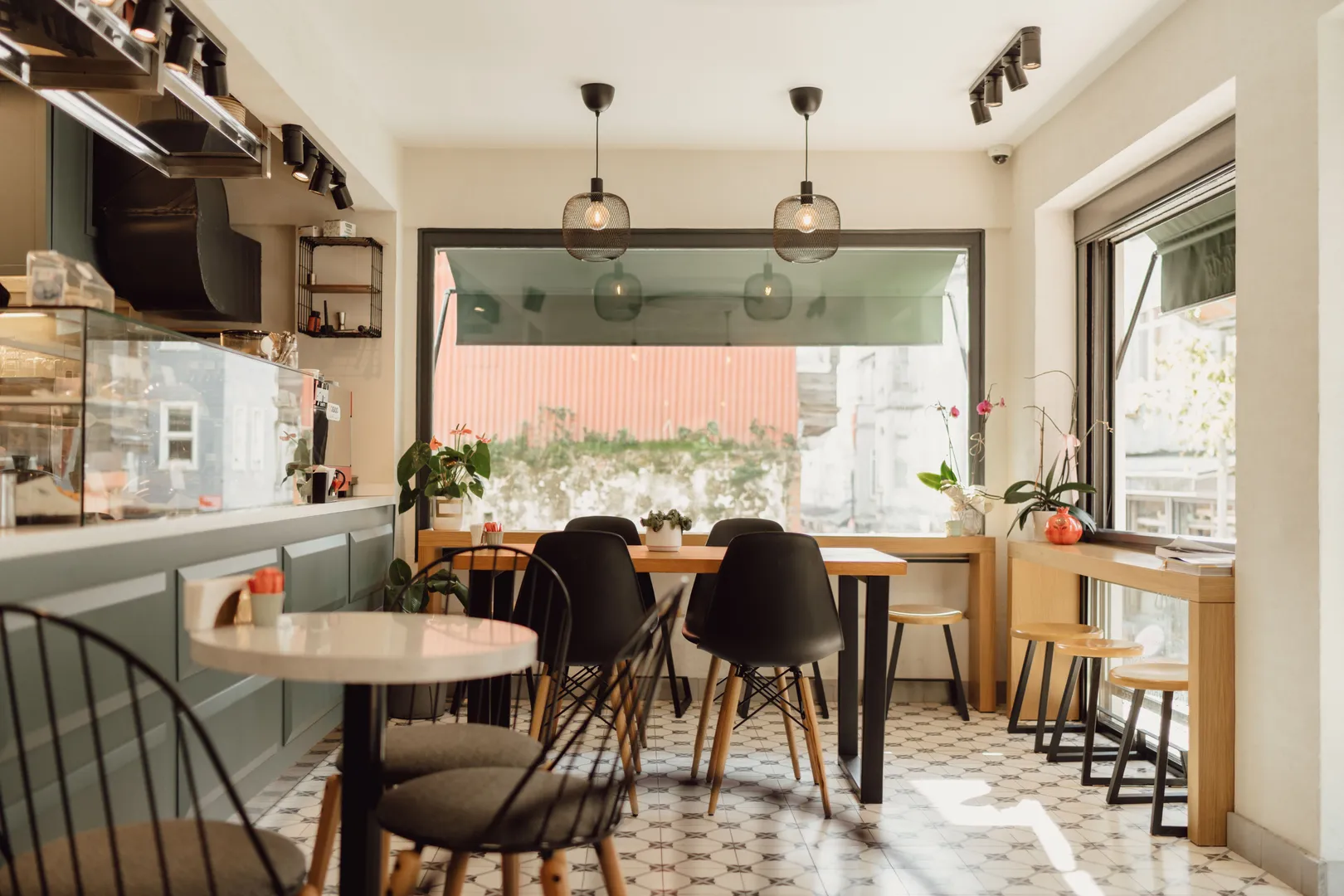 Salle intérieure d'un coffee shop avec tables, chaises et grande baie vitrée baignée de lumière naturelle.