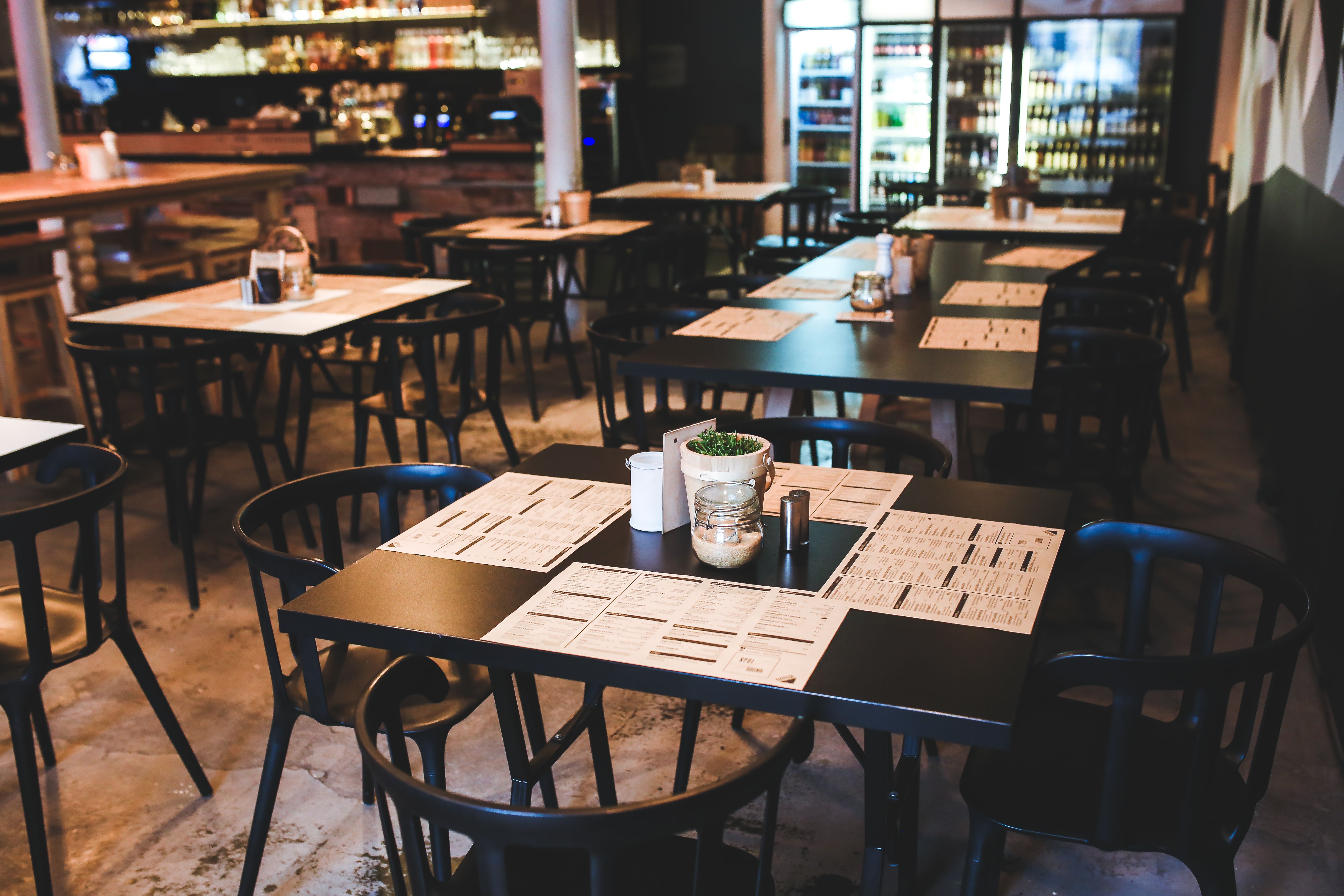 Salle de restaurant avec tables dressées de menus et bar en arrière-plan, avant le service.