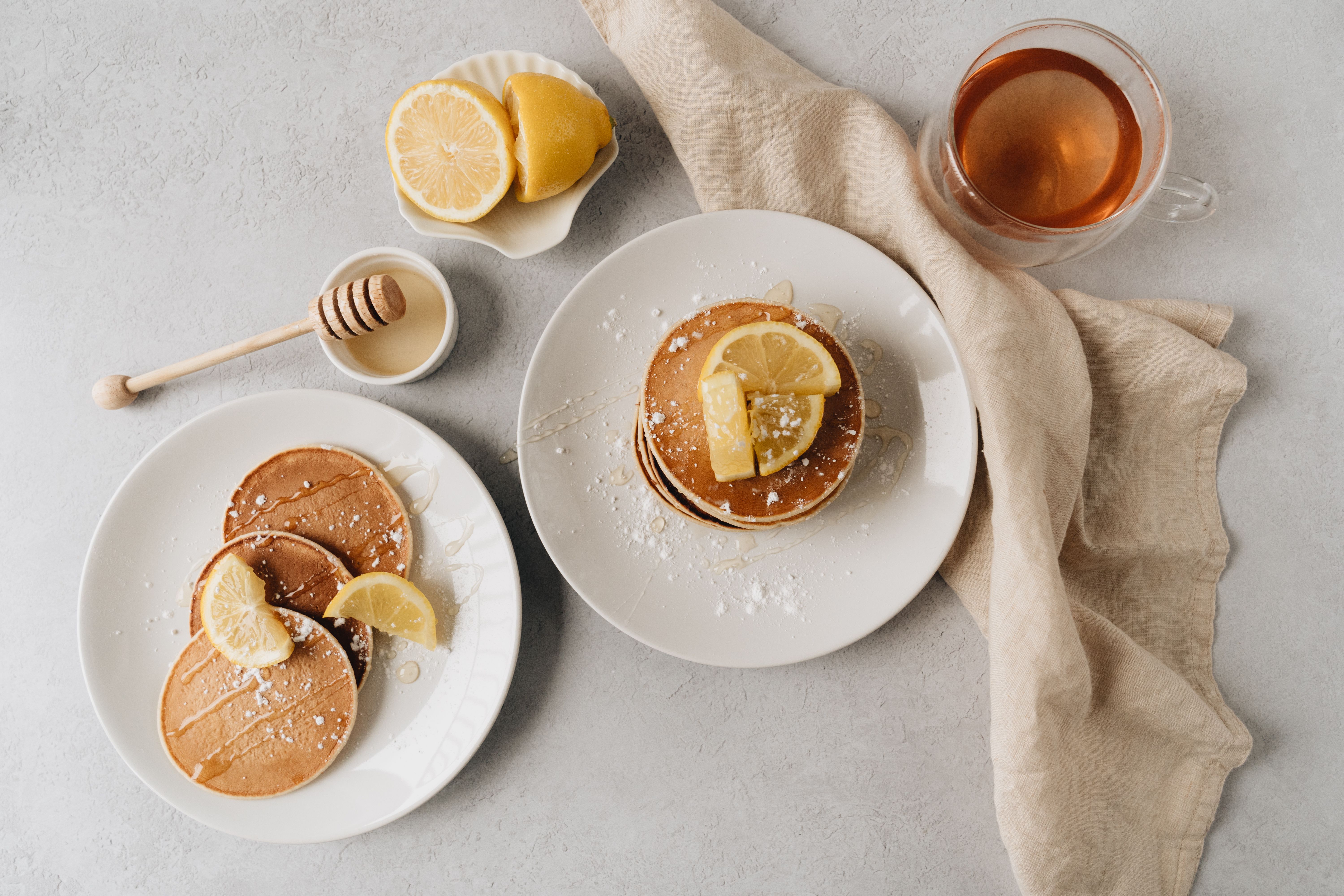 Assiettes de pancakes au miel et au citron accompagnées d'un thé, dressées pour un service petit-déjeuner ou brunch.