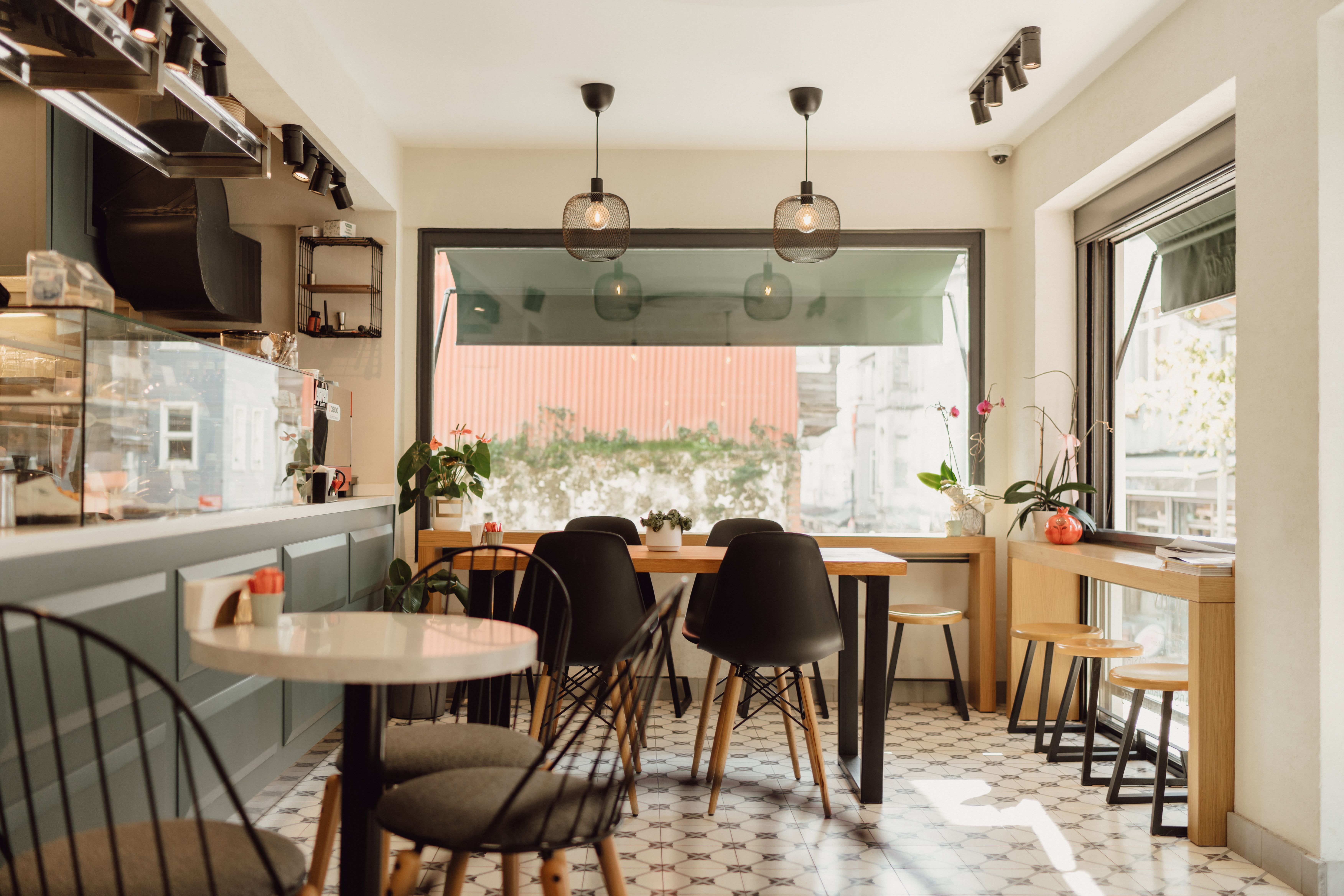 Salle intérieure d'un coffee shop avec tables, chaises et grande baie vitrée baignée de lumière naturelle.
